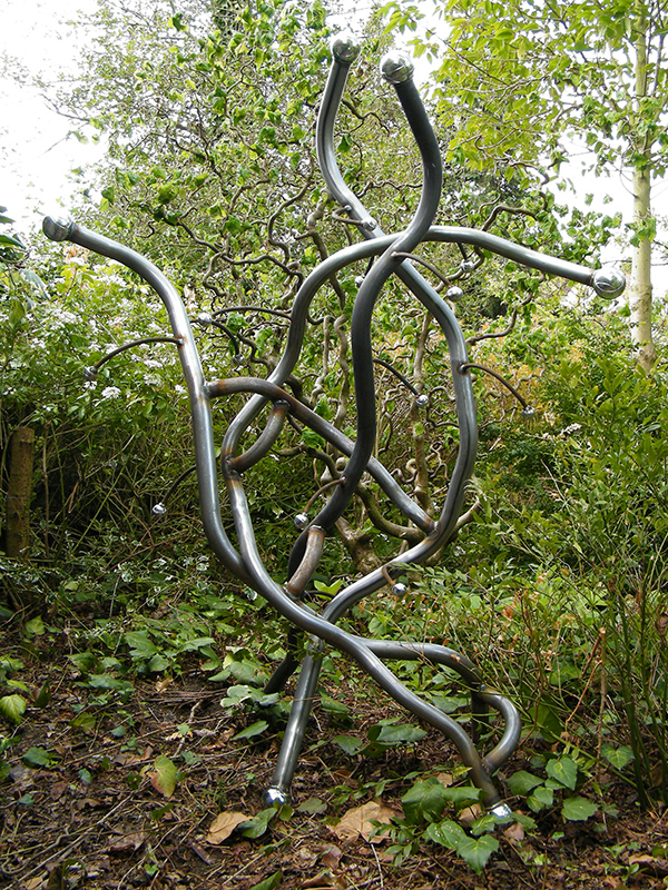 Metal sculpture titled Contorta viewed against a backdrop of Corkscrew Hazel